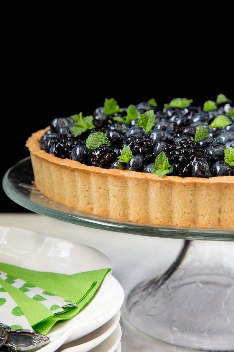 Vertical picture of lemon cheesecake with glazed berries on a glass cake stand on a black background