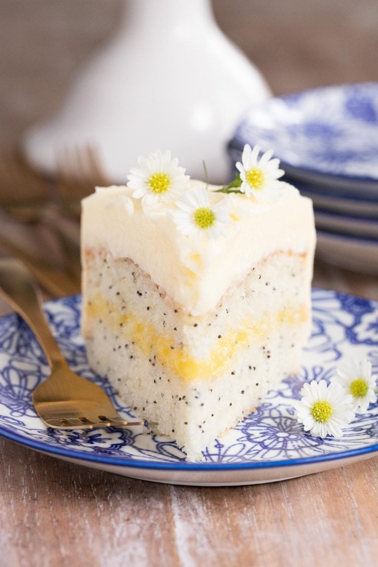Vertical picture of a slice of of Lemon Curd Poppy Seed Cake garnished with small flowers on a blue and white plate