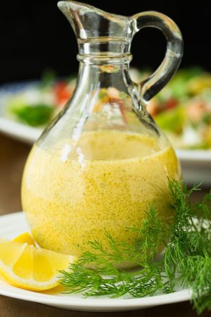 Vertical image of Lemon Dill Dressing in a glass cruet with fresh dill and lemon.