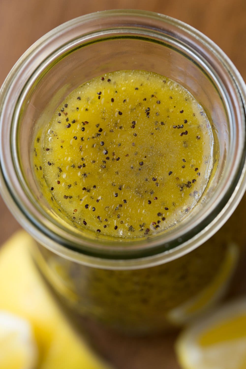Extreme closeup of the top of a carafe of Lemon Ginger Salad Dressing surrounded by lemon wedges.