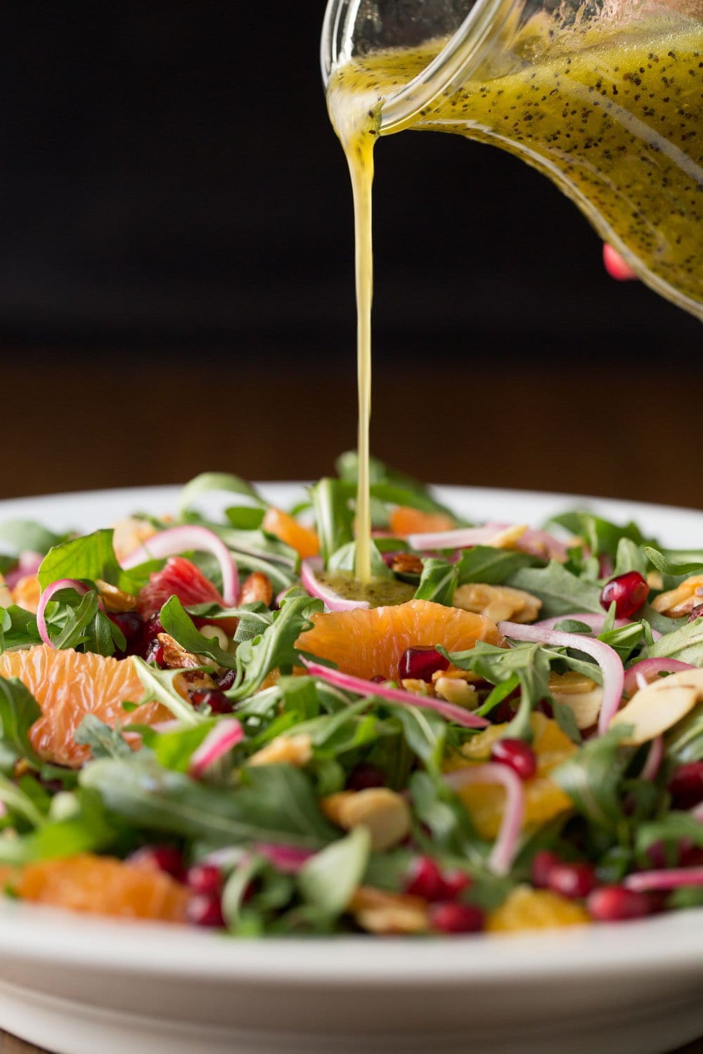 Photo of a fresh bowl of salad with Lemon Ginger Salad Dressing being poured over the salad from a glass carafe.
