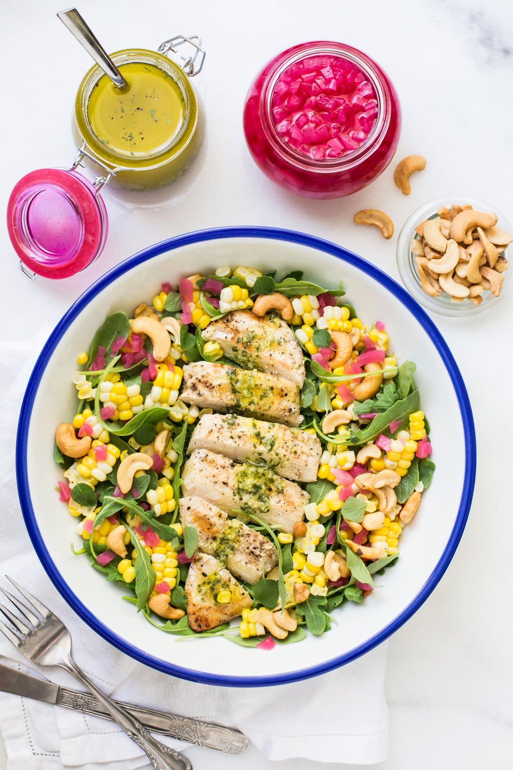 Overhead photo of Lemon Oregano Grilled Chicken Salad in a blue and white serving bowl with toppings and salad dressing on the side.