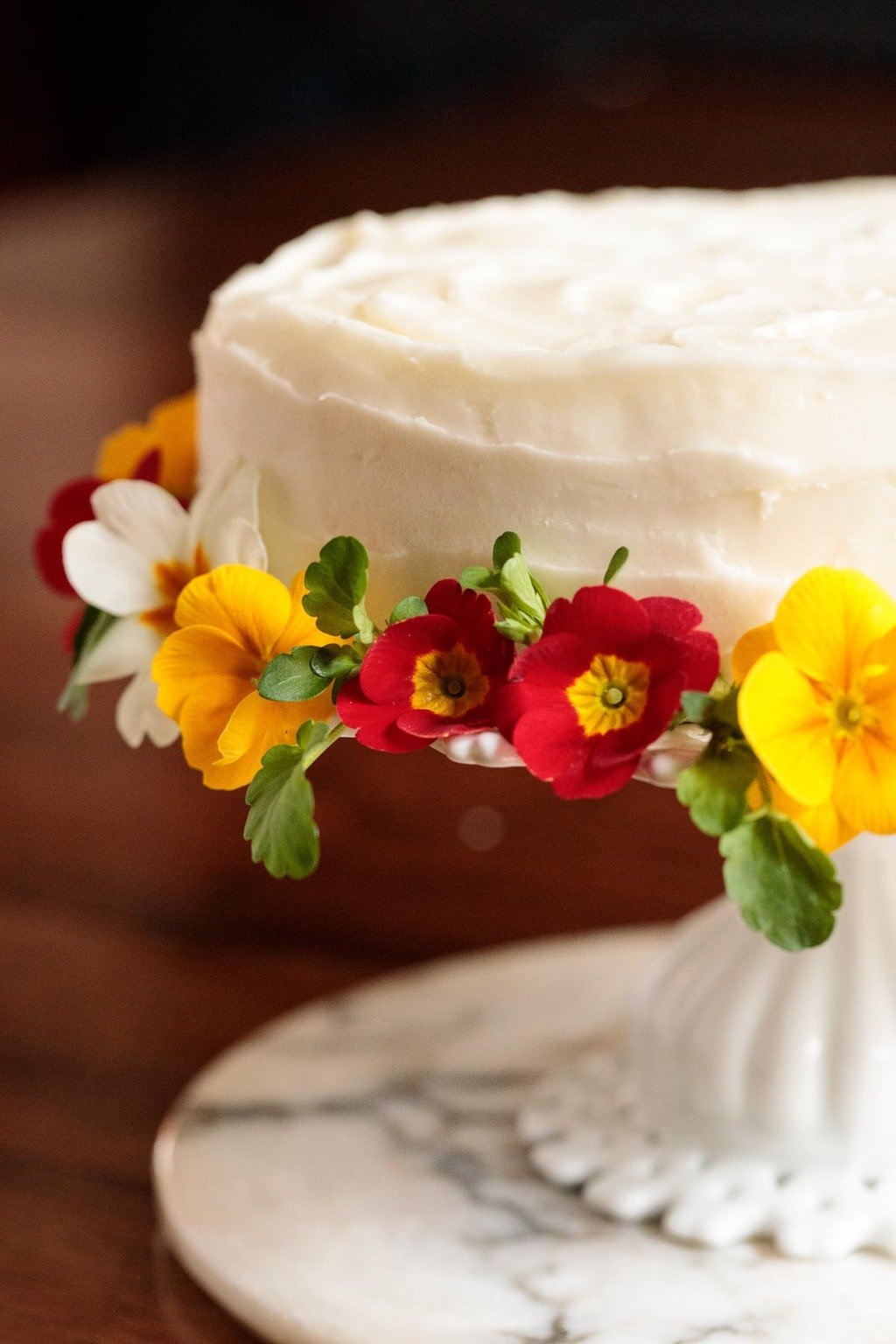 Vertical photo of a Lemon Ricotta Cake on a white cake on a wood farm table.