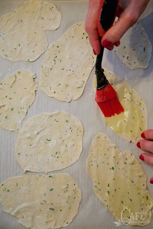 Overhead process photo of a person brushing the thinly rolled dough with olive oil for making Lemon Rosemary Flatbread Crackers.