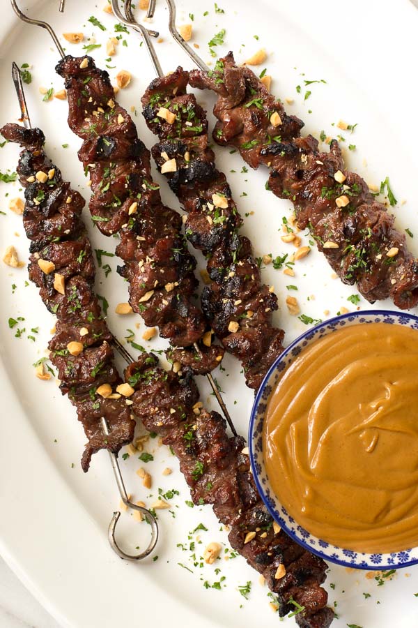 Overhead photo of Lemongrass Beef Skewers with a dish of peanut dipping sauce on a white platter.