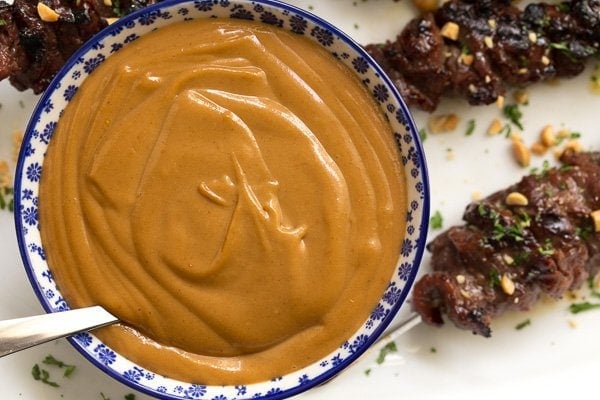 Closeup overhead photo of a bowl of Easy Peanut Sauce on a white platter with Grilled Lemongrass Beef Skewers.