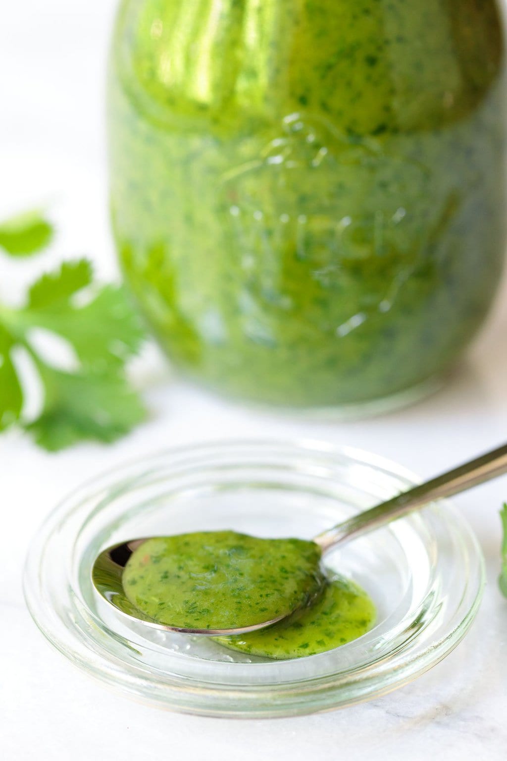 Photo of a spoonful of Lemongrass Cilantro Salad Dressing with a glass jar full of the dressing in the background with fresh cilantro.