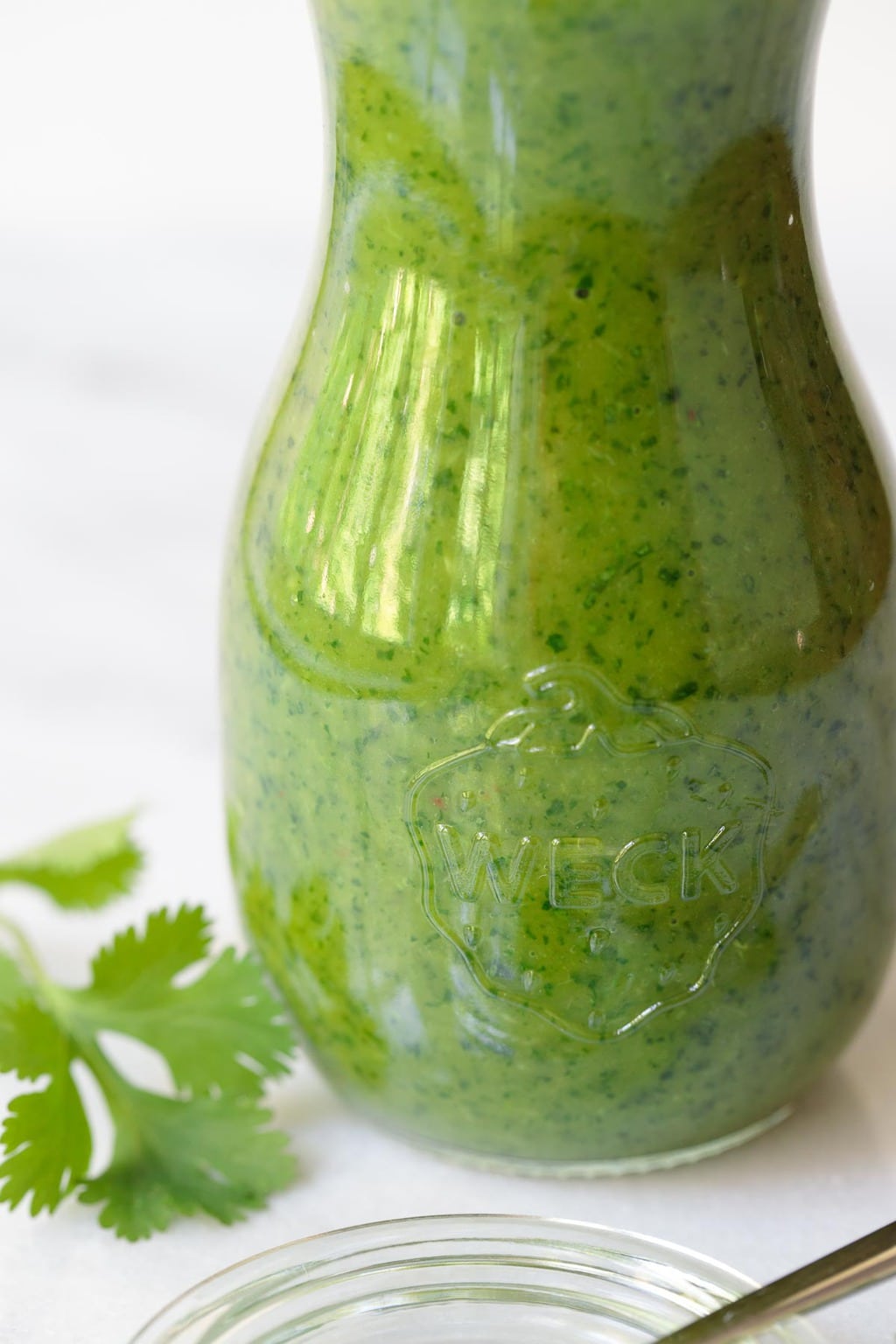 Photo of a glass jar of Lemongrass Cilantro Salad Dressing with a spoonful of the sauce in the foreground.