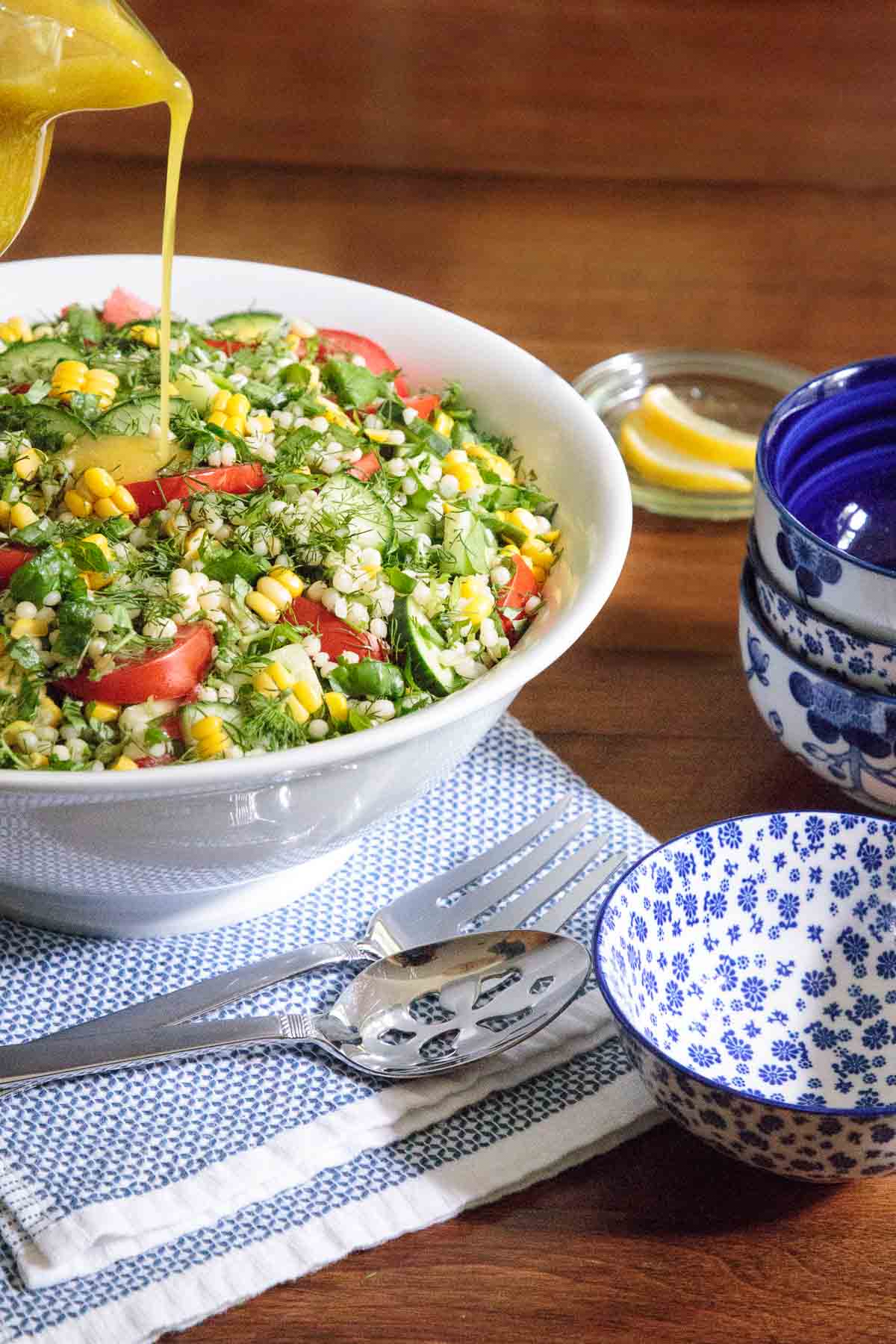 Vertical photo of a Lemony Mediterranean Couscous Salad in a white serving bow with dressing being poured over the top.
