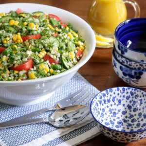 Vertical picture of lemony couscous salad in a white bowl on a wooden table with small blue and white bowls stacked