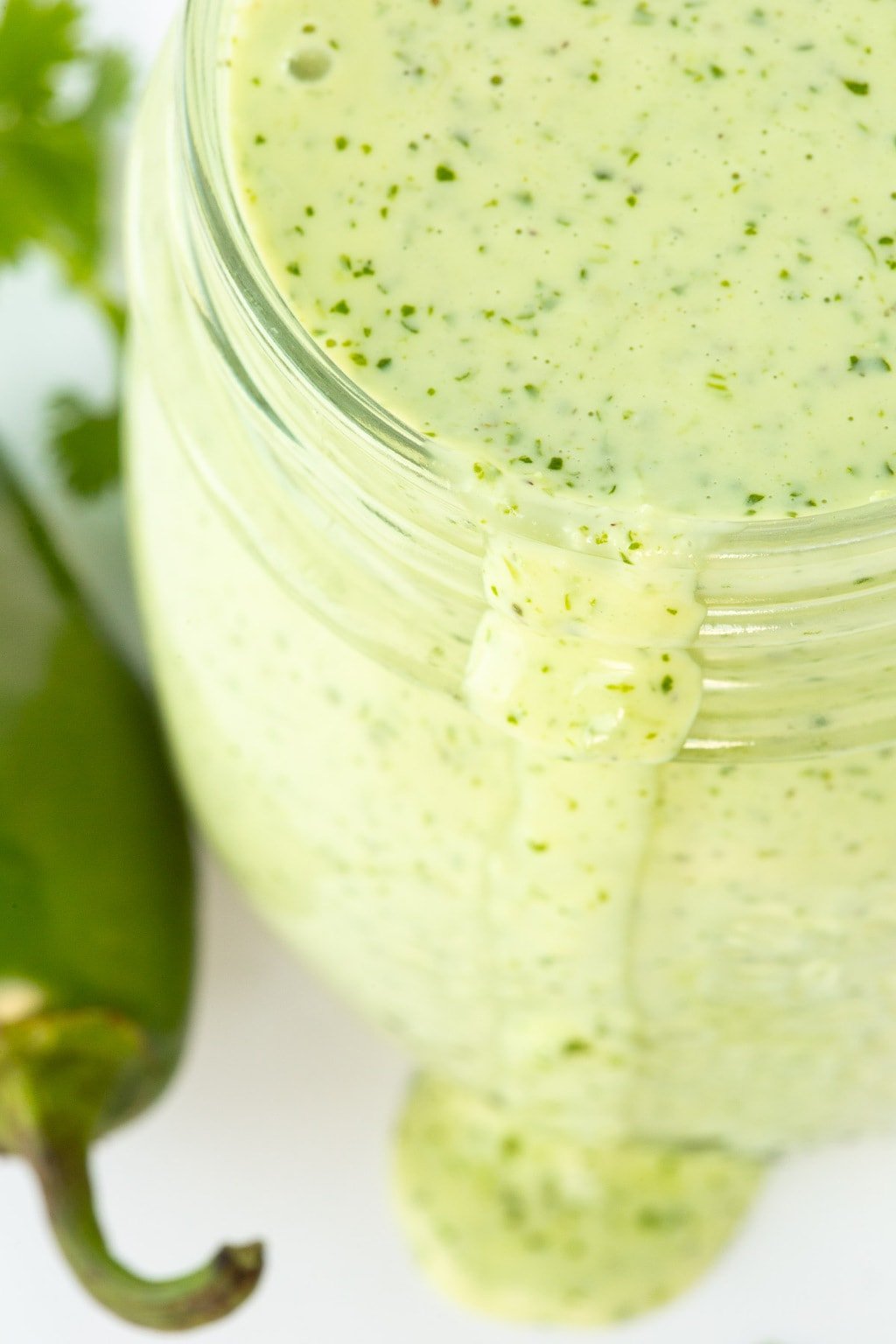 Vertical ultra closeup photo of a glass jar of Light and Spicy Southwestern Cilantro Buttermilk Dressing.