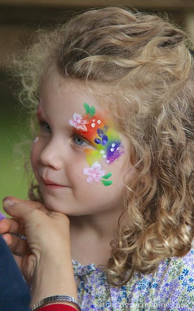 Lilly with her face painted with a rainbow and colorful flowers.