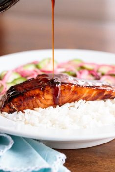 Vertical closeup photo of Make Ahead Honey Coriander Salmon on a bed of rice with sauce being poured over it.