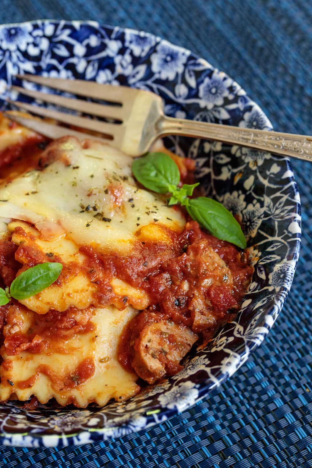 Photo of a serving of Italian Chicken Sausage Ravioli Lasagna in a blue and white patterned bowl garnished with basil leaves.