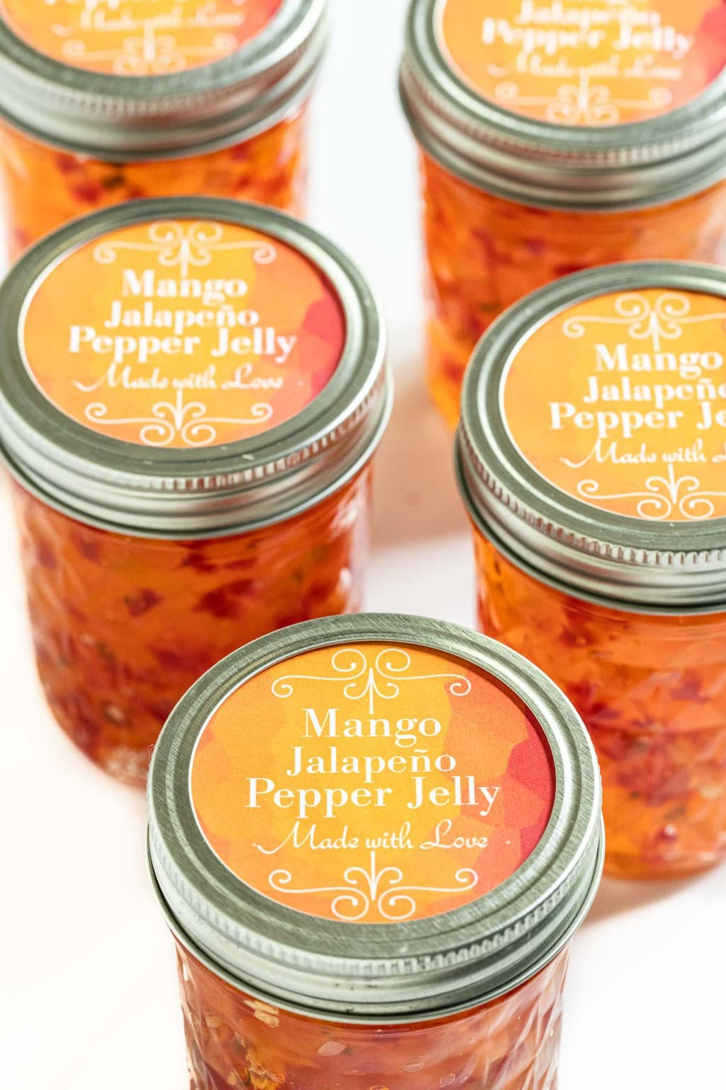 Vertical photo of jars of Mango Jalapeño Pepper Jelly with printed labels on the top of each jar identifying them as "Mango Jalapeño Pepper Jelly.