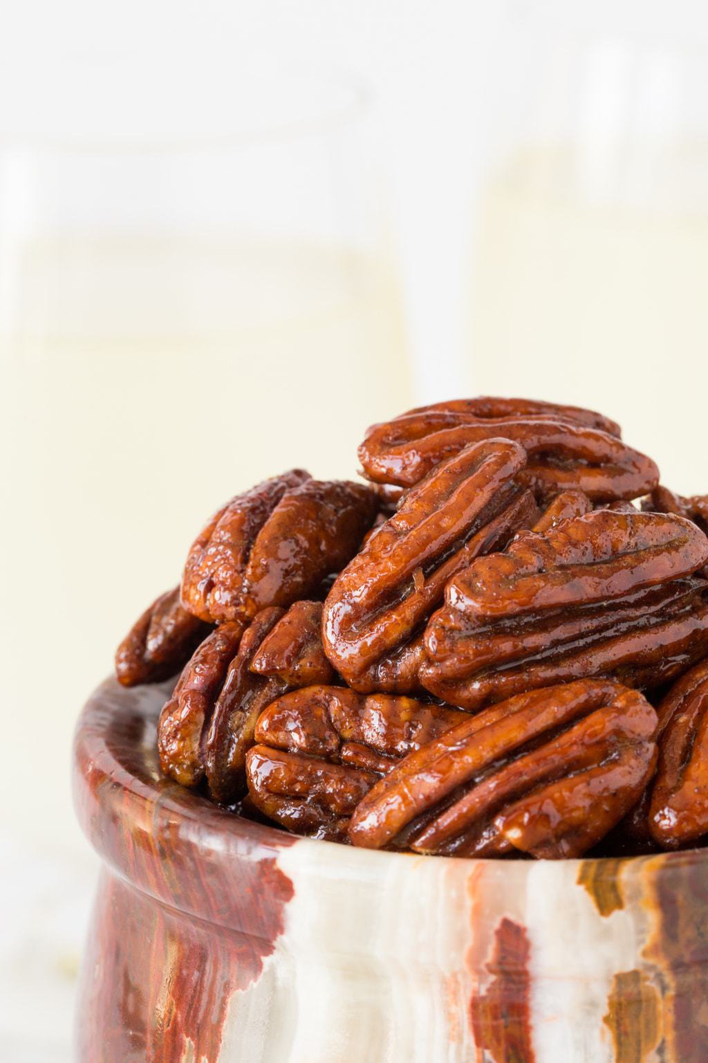 Vertical closeup photo of Maple Molasses Glazed Pecans in a small marble bowl.
