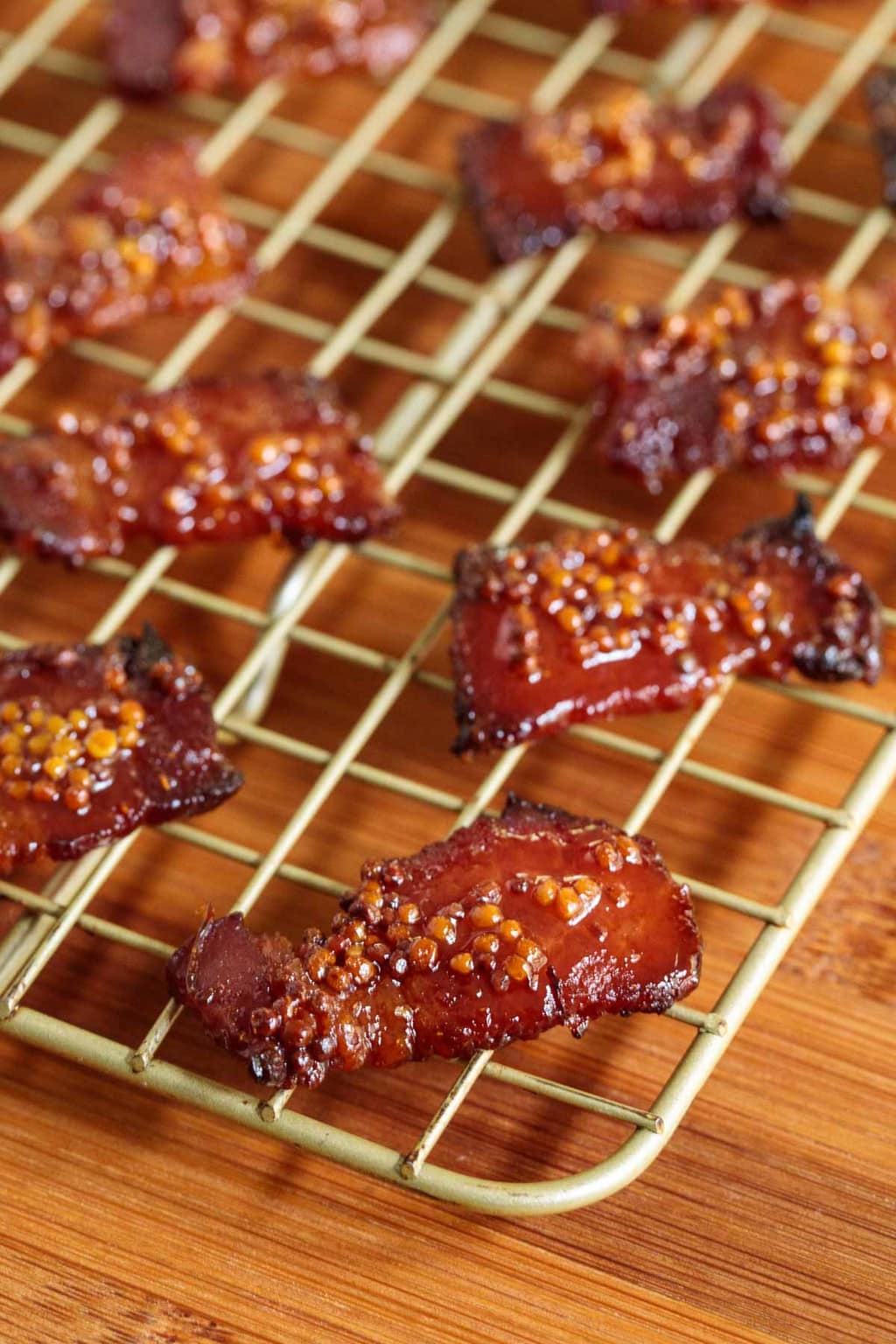 Closeup photo of a baking rack filled with Maple Mustard Candied Bacon on a wood cutting board.