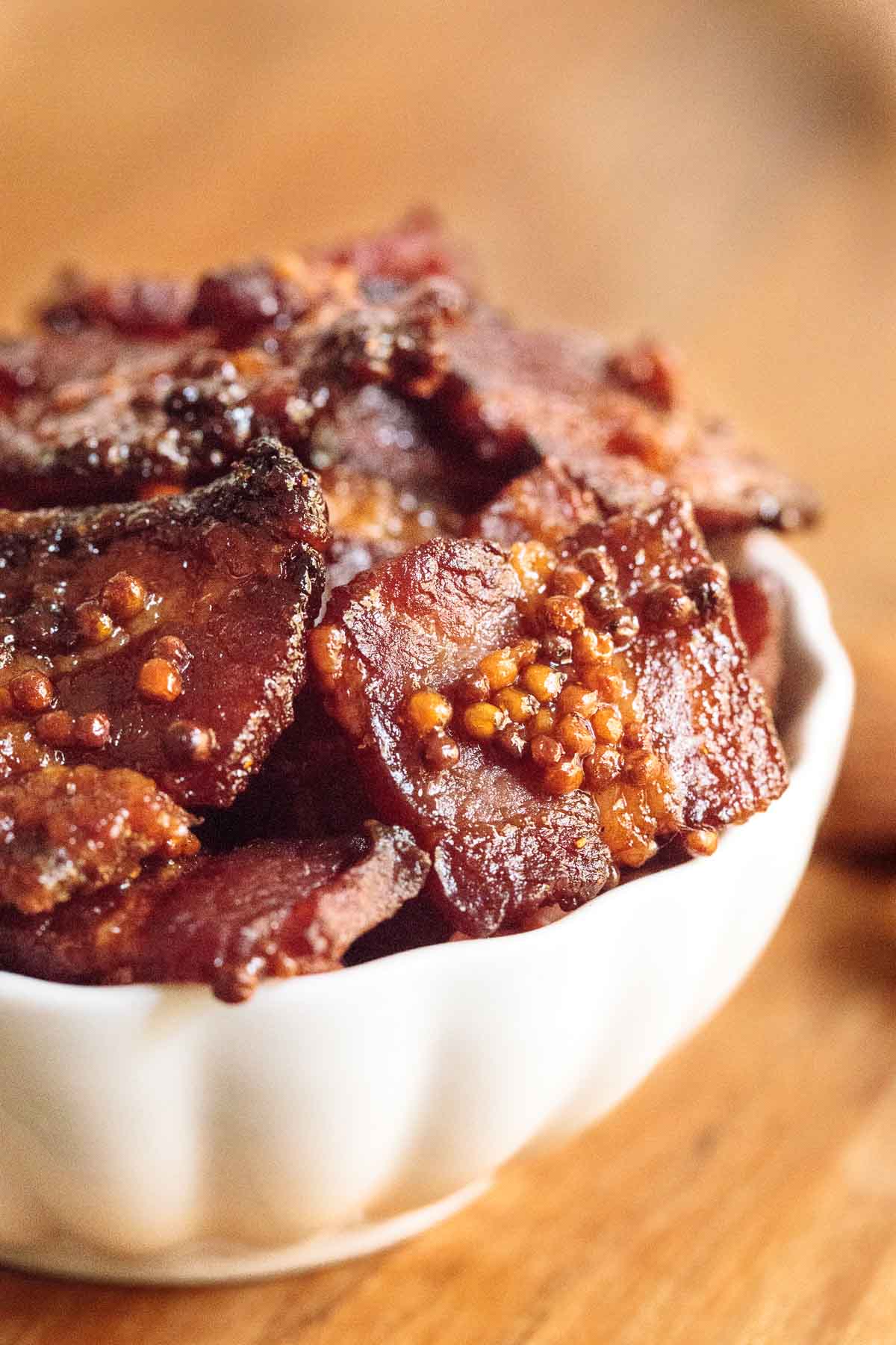 Vertical closeup photo of Maple Mustard Candied Bacon in a white serving bowl.