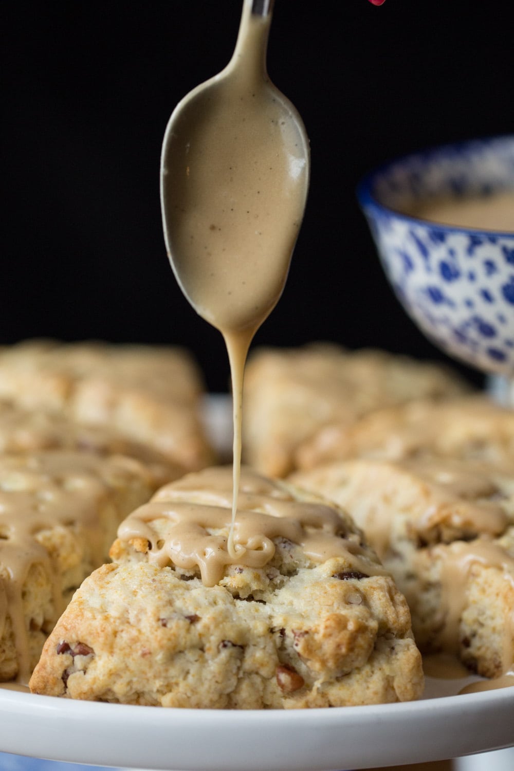 Vertical photo of a plate of Ridiculously Easy Maple Pecan Scones with the front scone being covered in maple glaze with a spoon.