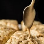 Close up vertical picture of Maple Pecan Scones on a platter with a spoon drizzling glaze over top