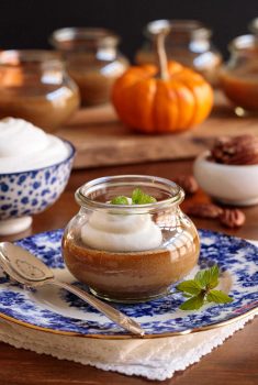Vertical closeup photo of Maple Pumpkin Pots de Creme with whipped cream on a blue and white patterned plate.