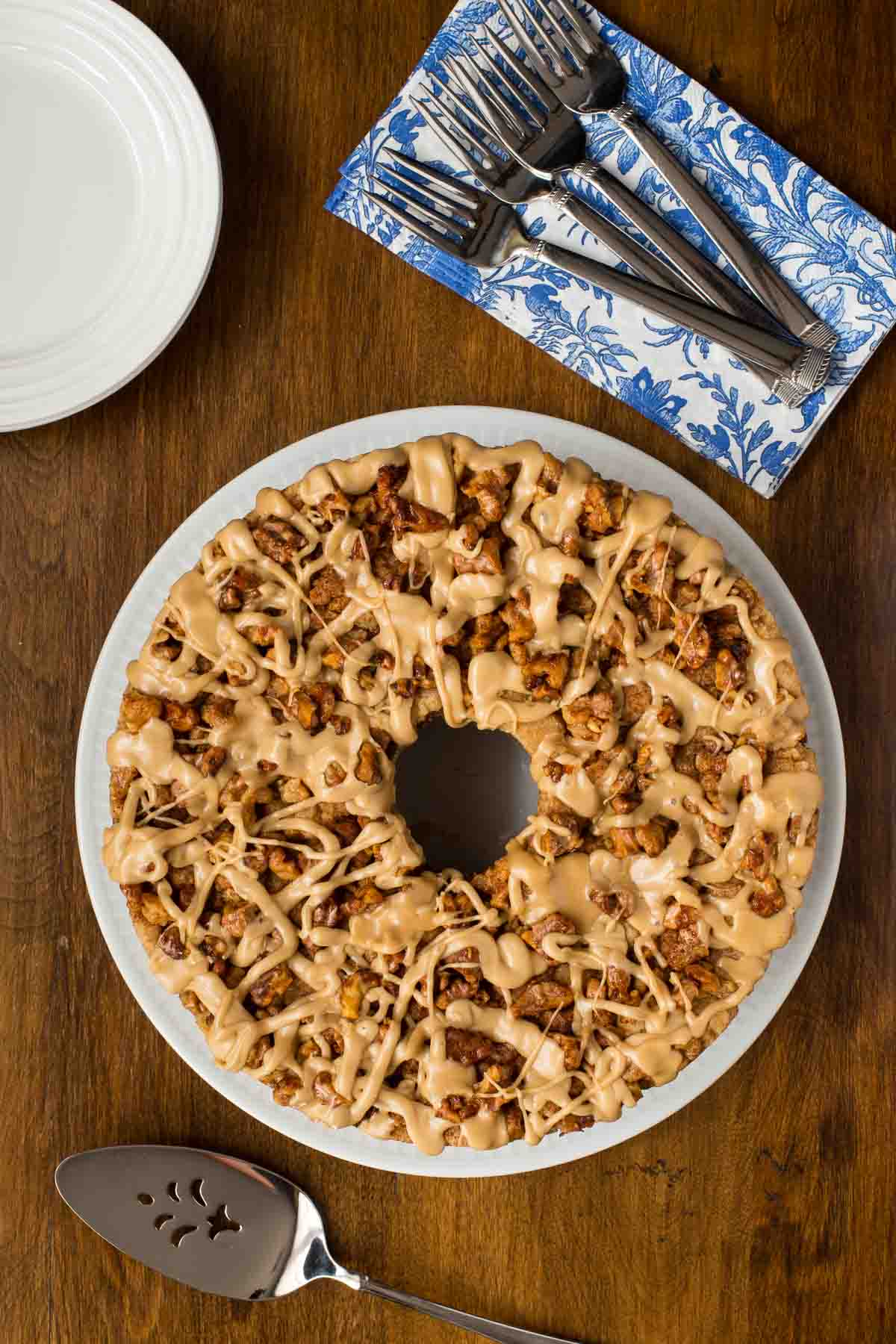 Overhead photo of a Maple Walnut Banana Coffee Cake on a white plate with serving utensils nearby.