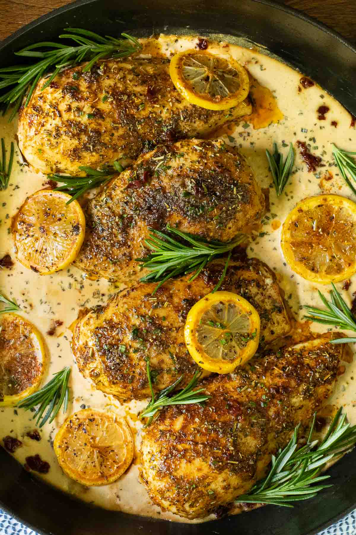 Overhead vertical photo of a skillet filled with Marry Me Chicken and garnished with sliced roasted lemons and fresh rosemary sprigs.