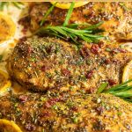 Vertical closeup photo of a skillet of Marry Me Chicken garnished with roasted lemons and fresh rosemary sprigs.