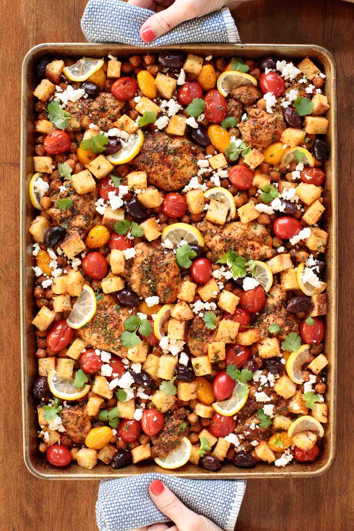Overhead vertical photo of Mediterranean Sheet Pan Chicken on a wood table.