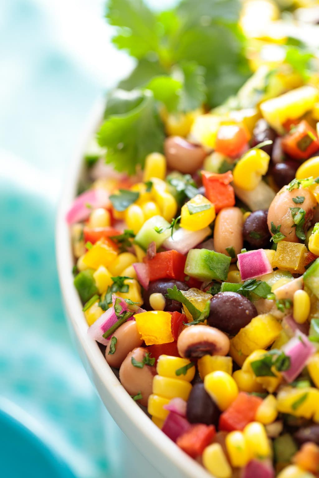 Closeup of a white serving bowl of Mexican Corn and Bean Salad surrounded by a turquoise napkin.