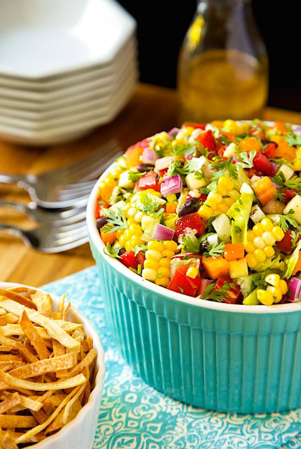 Photo of a turquoise bowl filled with Mexican Chopped Salad with crisp tortilla strips in a dish in the foreground.