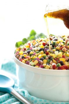 Vertical picture of Mexican Corn and Bean Salad in a white bowl with dressing being poured on top