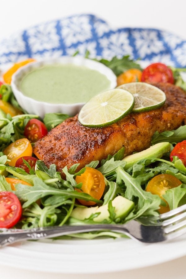 Photo of a Mexican Sugar-Seared Salmon Salad on a white serving plate with a small side dish of Spicy Cilantro Buttermilk Dressing in the background.