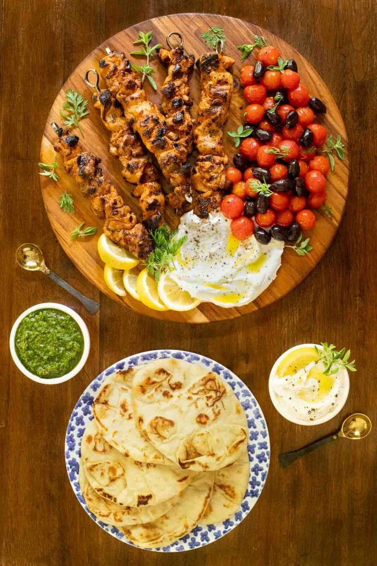 Vertical overhead picture of Middle Eastern Grilled Chicken on a platter with pita bread and sauces