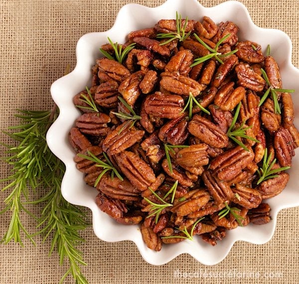 Overhead photo of a white dish of Sweet and Spicy Roasted Pecans on a tan woven placemat.