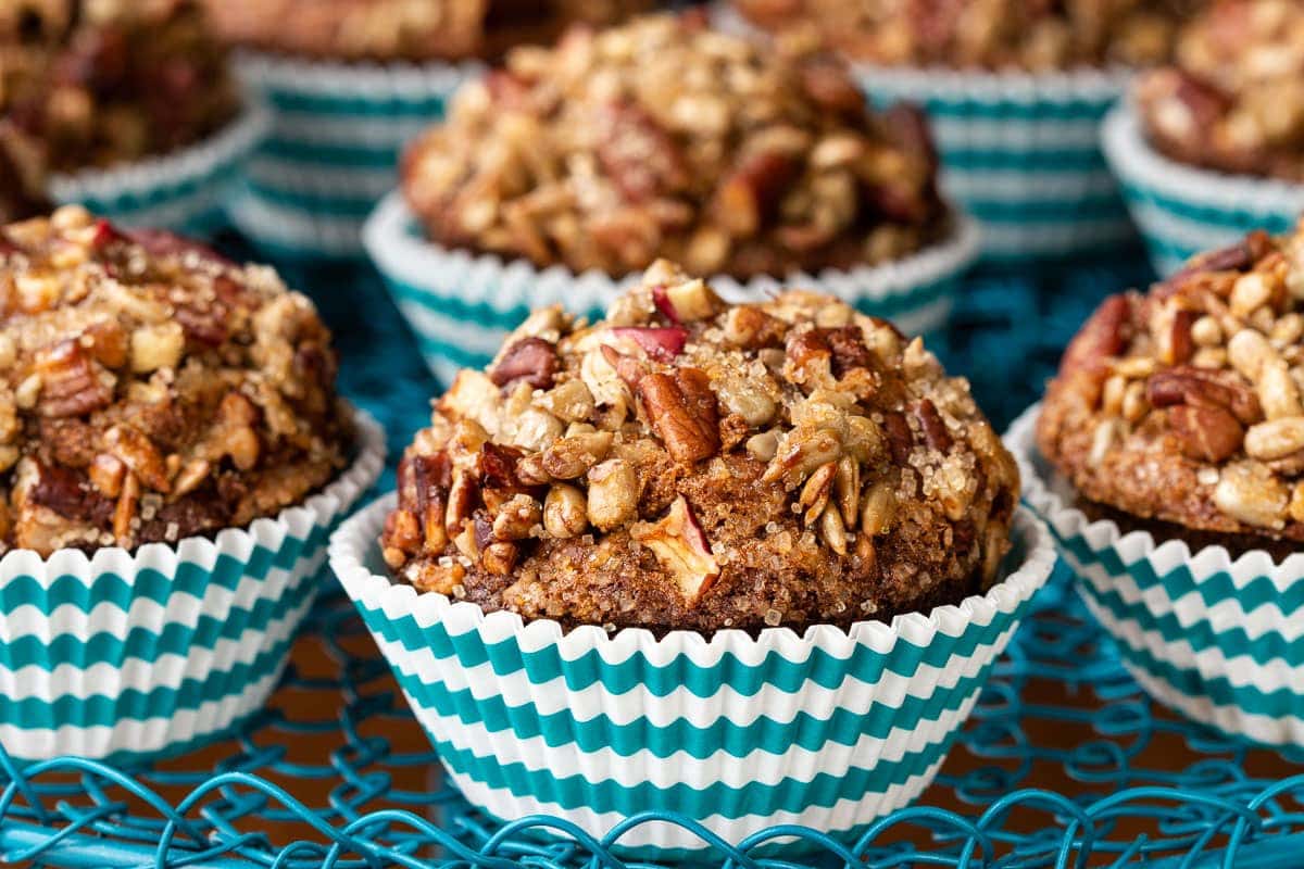 Horizontal closeup photo of a batch of Candied Pecan Morning Glory Muffins in turquoise striped muffin cups.