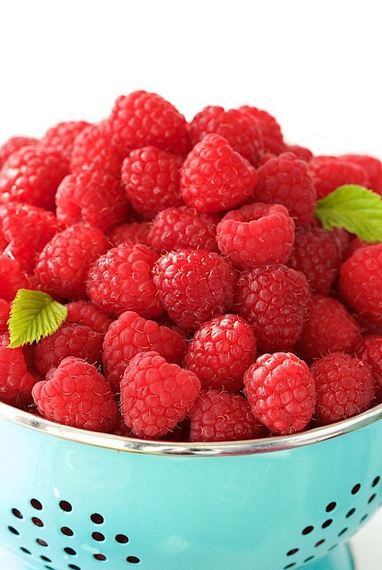 A closeup photo of a colander overflowing with fresh raspberries.