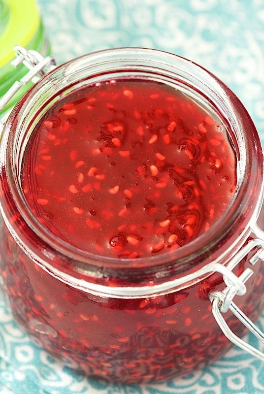 Overhead photo of a glass jar of Old Fashioned Raspberry Preserves on a turquoise napkin.