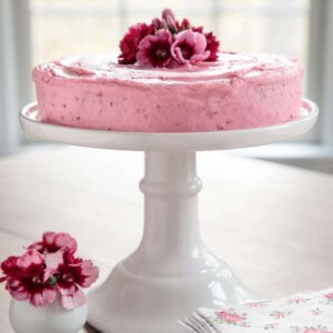 Vertical picture of one bowl buttermilk cake with raspberry buttercream icing on a white cake stand
