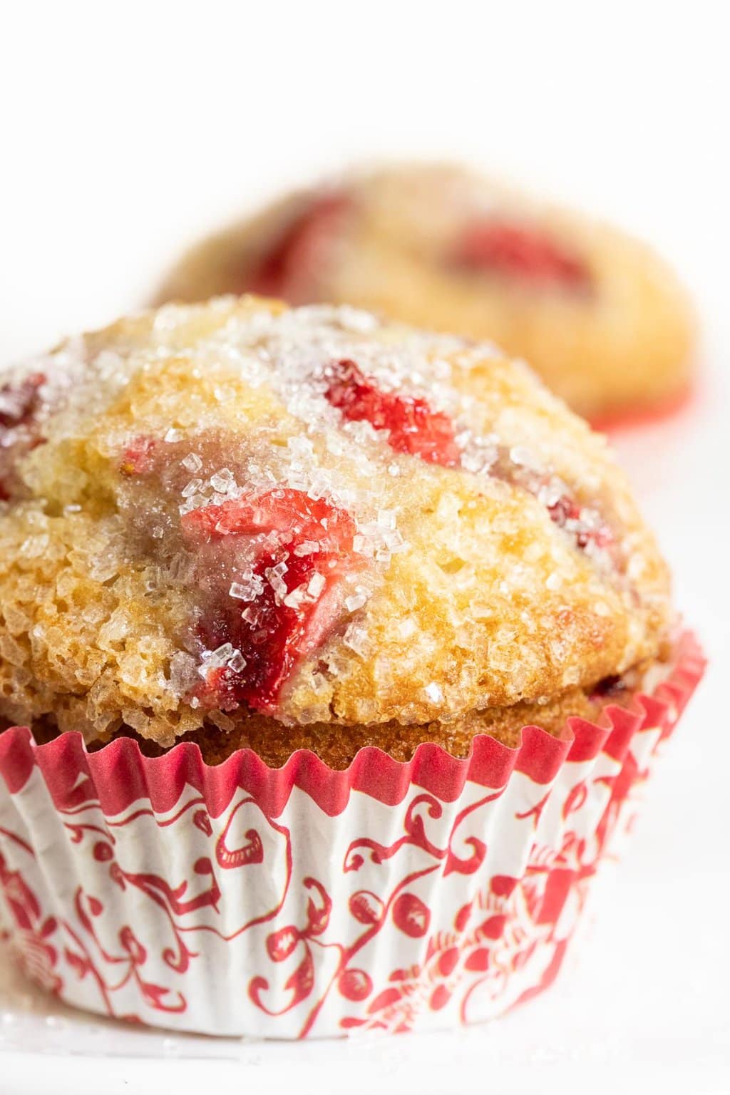 Extreme vertical closeup photo of a Fresh Strawberry Buttermilk Muffin in a red and white patterned cupcake liner.