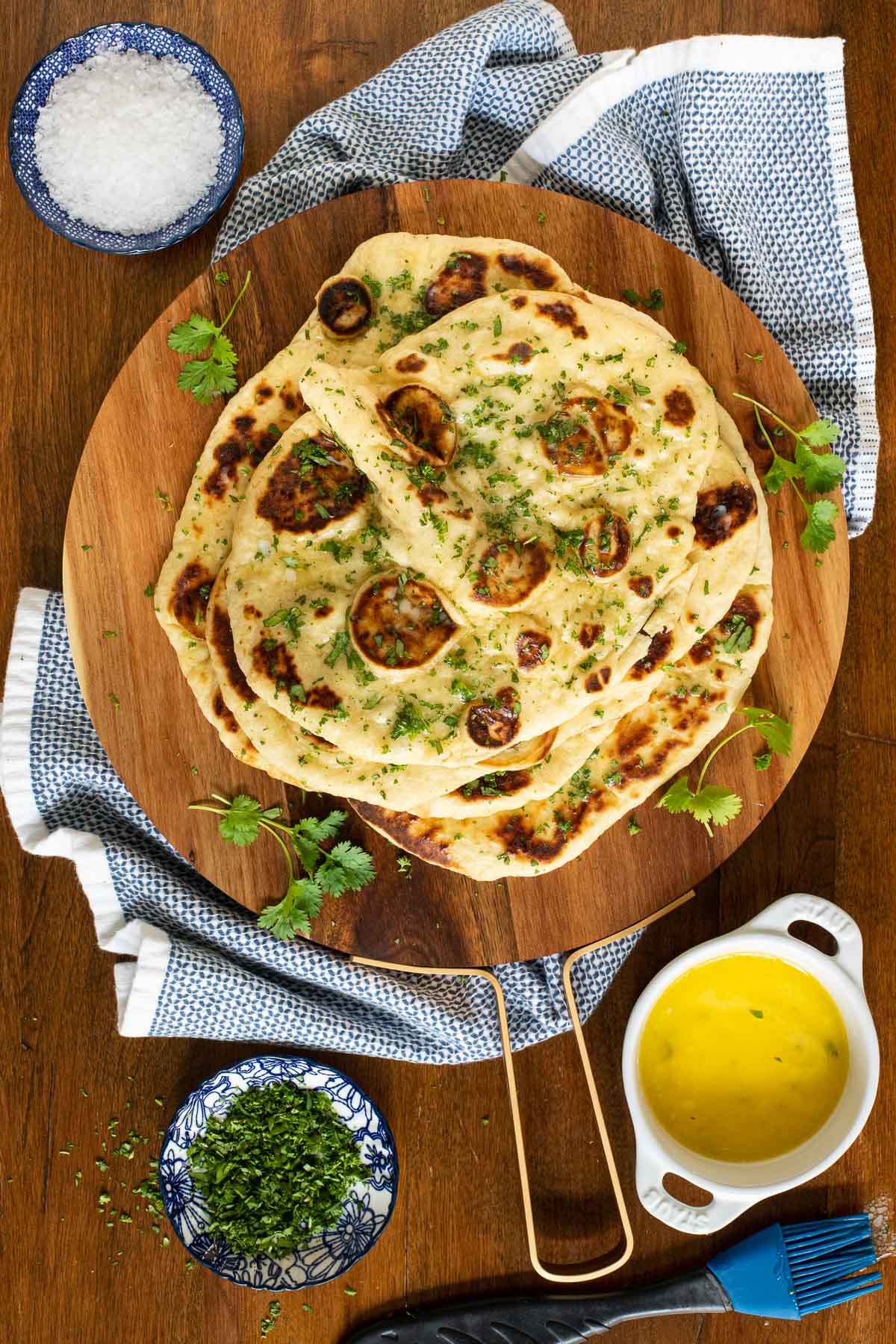Overhead vertical photo of One-Bowl, No-Mixer Naan on a wooden cutting board with herbs and butter.