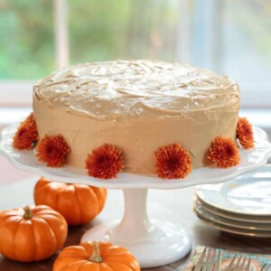 Vertical picture of one bowl pumpkin cake on a white cake stand, decorated with orange flowers and small pumpkins