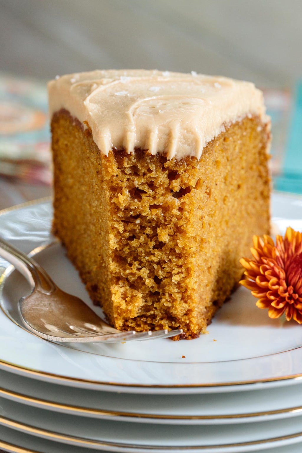 Closeup photo of a slice of One-Bowl Pumpkin Cake with Salted Caramel Icing on a white with gold trim serving plate.