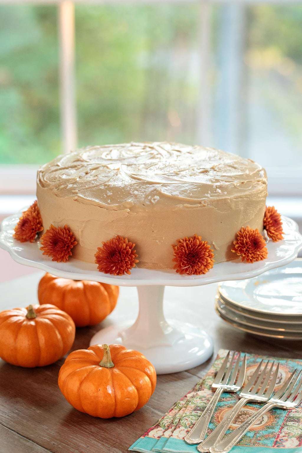 Vertical photo of one bowl pumpkin cake on a white cake stand, decorated with orange flowers and mini pumpkins.