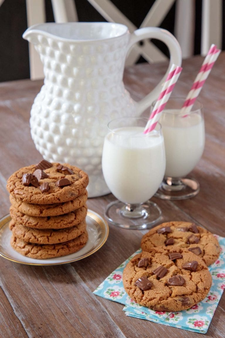 Reeses peanut butter cookies on a wooden table with napkins and glasses of milk.