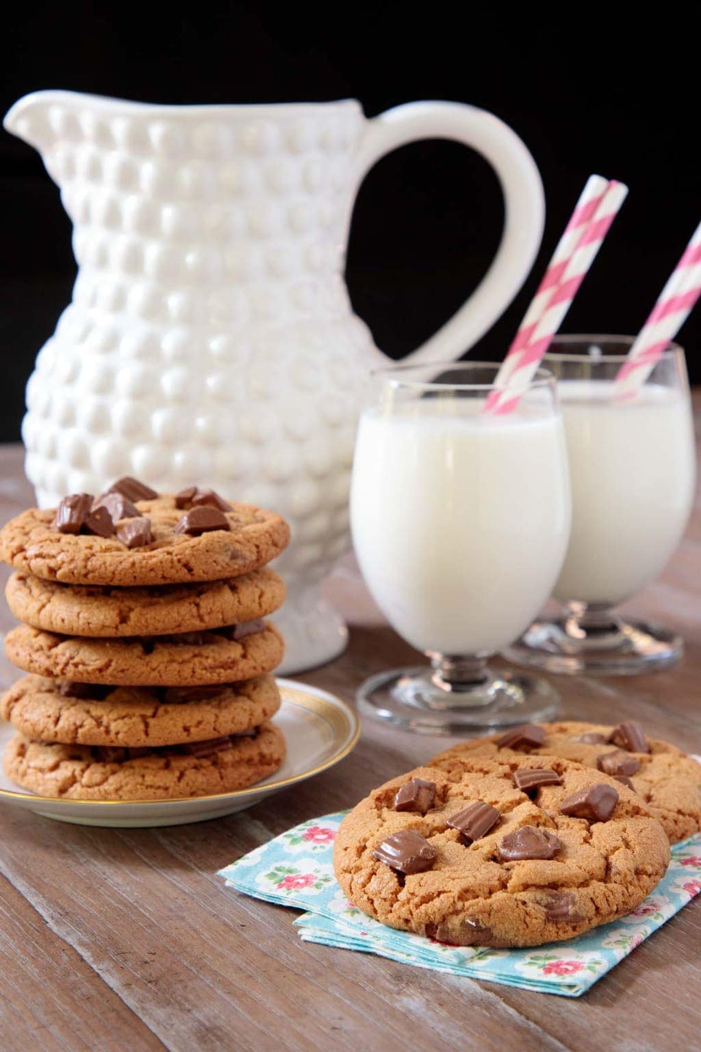 Vertical photo of a batch of One-Bowl Reese's Peanut Butter Cookies with a pitcher and glasses of milk in the background.