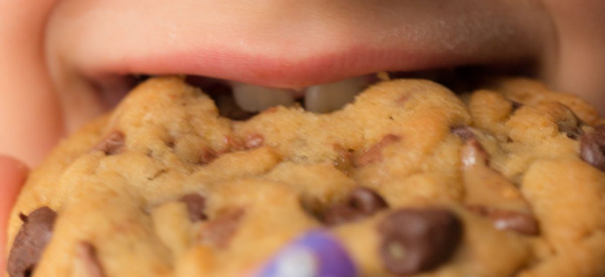 A super closeup of a young girl's face biting into a One Bowl Toffee Bar Chocolate Chip Cookie