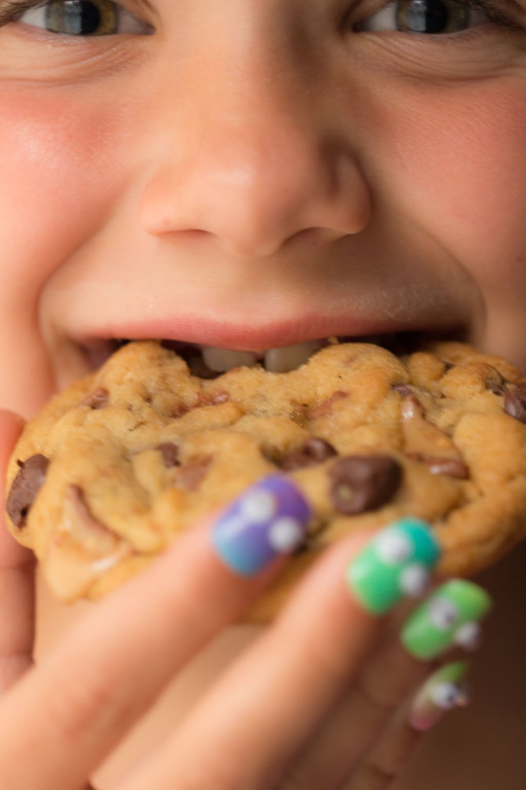 A super closeup of a young girl's face biting into a One Bowl Toffee Bar Chocolate Chip Cookie
