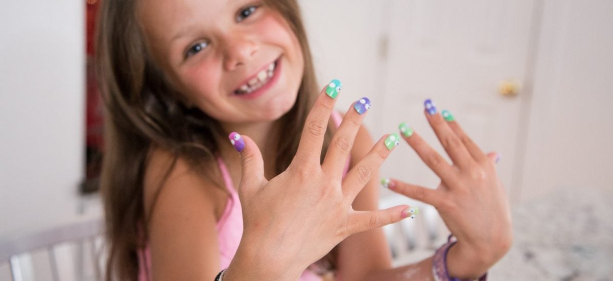 A shot of a young girl baker showing off her brightly colored finger nails with flour on her arm from making cookies.