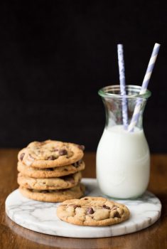 Vertical picture of Toffee Bar Chocolate Chip cookies stacked on a platter with a glass of milk and straws